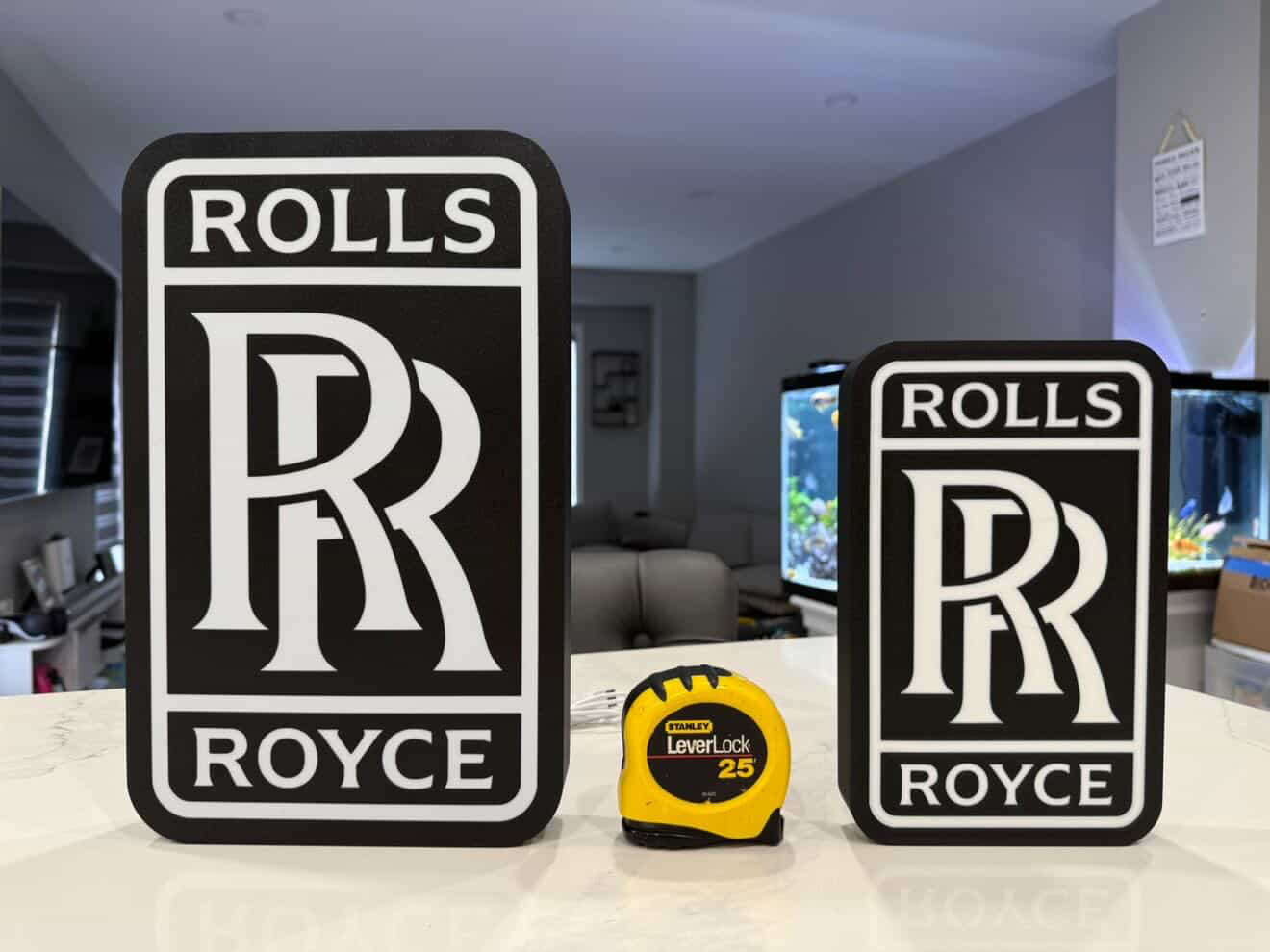 Two Rolls-Royce lightboxes side by side, larger 14-inch sign on the left and smaller 10-inch sign on the right, with a tape measure between them