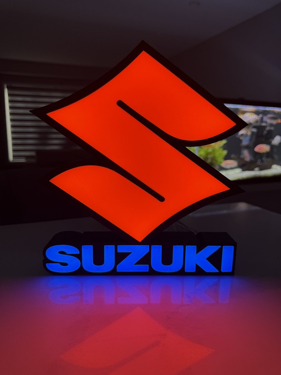Red Suzuki emblem above glowing blue Suzuki lettering